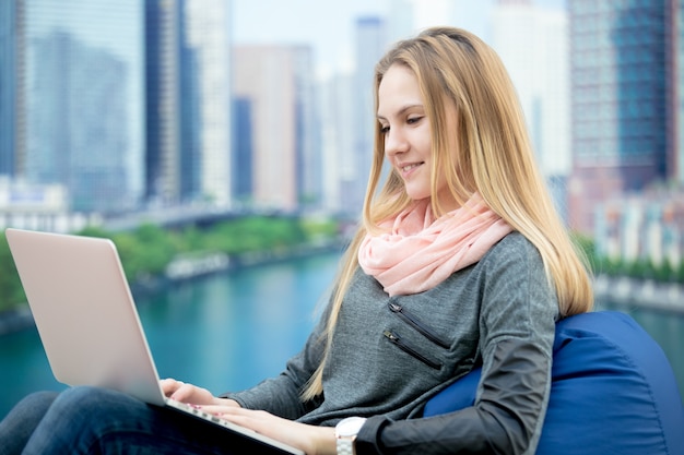 Rapariga sentada com laptop, paisagem urbana no fundo