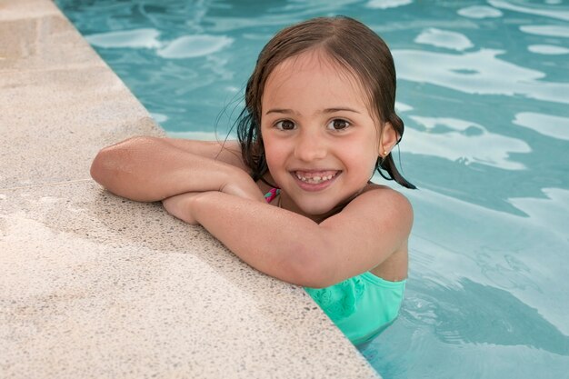 Rapariga sorridente com tiro médio a posar na piscina