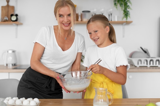 Rapariga sorridente e mulher a cozinhar em tiro médio