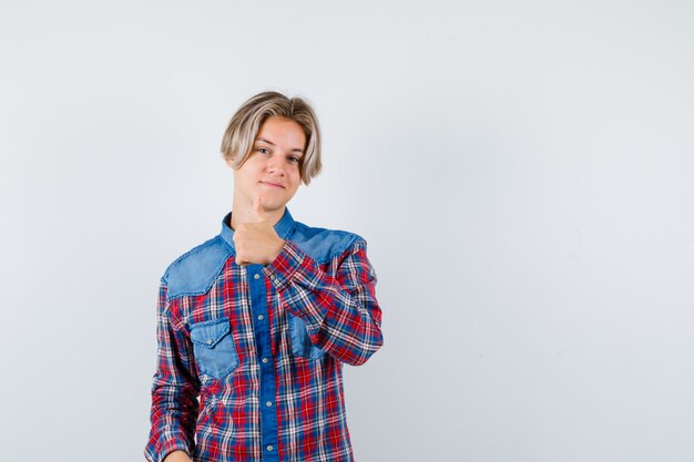 Rapaz adolescente com camisa quadriculada, aparecendo o polegar e parecendo satisfeito, vista frontal.