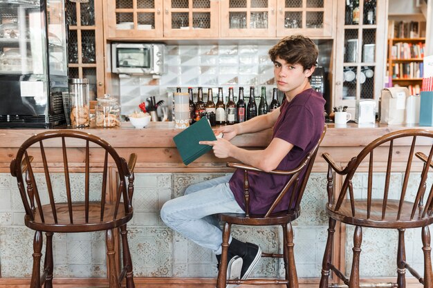 Rapaz adolescente com livro perto de balcão vintage no café