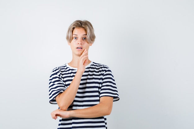 Foto grátis rapaz adolescente, mantendo a mão no queixo em t-shirt e parecendo preocupado. vista frontal.