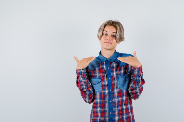 Foto grátis rapaz adolescente mostrando gesto de altura na camisa quadriculada e parecendo alegre. vista frontal.