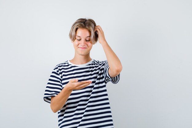 Rapaz adolescente olhando para as palmas das mãos, coçando a cabeça na camiseta e parecendo alegre. vista frontal.