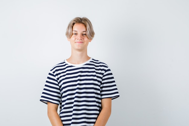 Foto grátis rapaz adolescente posando em pé em uma t-shirt e parecendo satisfeito. vista frontal.