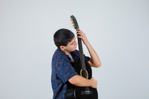 Foto grátis rapaz adolescente segurando uma guitarra no peito com uma camiseta e parecendo confiante