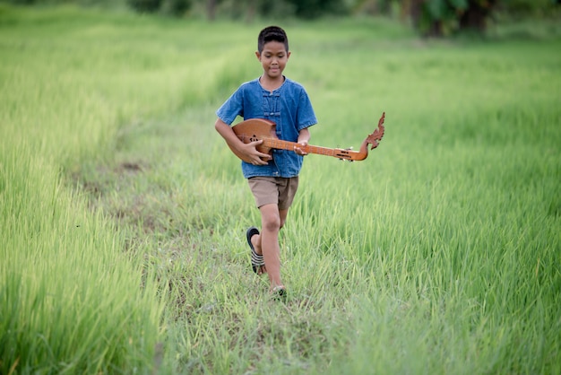 Rapaz asiático com guitarra artesanal no exterior, país de vida