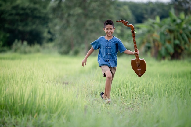 Rapaz asiático com guitarra artesanal no exterior, país de vida