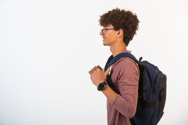 Foto grátis rapaz de cabelo encaracolado com óculos opticos segurando a mochila e indo para a esquerda