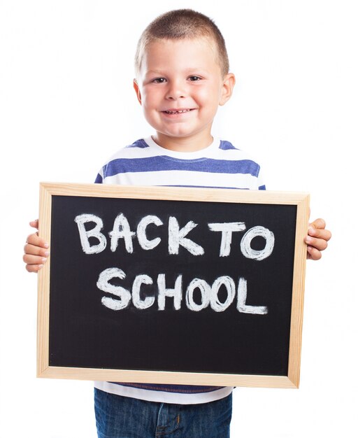 Rapaz pequeno que sorri com um quadro-negro com a mensagem &quot;de volta à escola&quot;