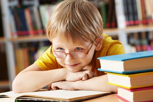 Rapaz pequeno que sorri na biblioteca