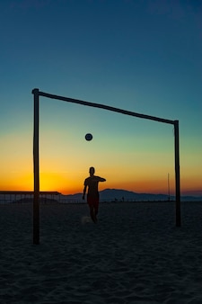 rapaz praticando esportes com bola na praia em pleno pôr do sol de verão na costa brasileira