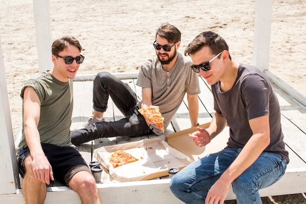 Foto grátis rapazes jovens com pizza descansando na praia