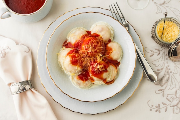 Ravioli com molhos de tomate e queijo ralado na tigela de cerâmica contra a toalha de mesa