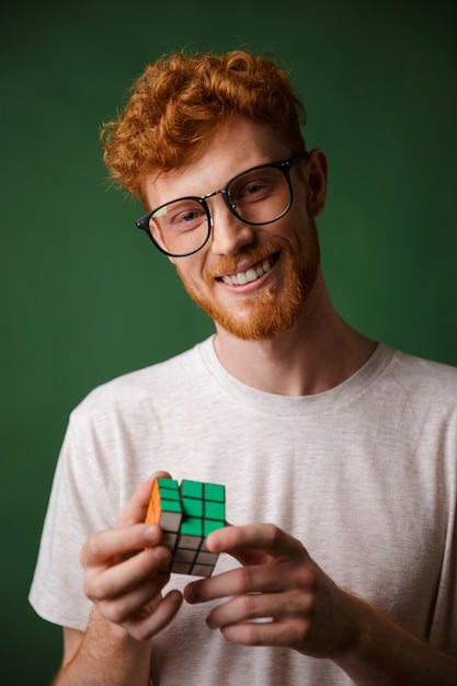 Readgead inteligente jovem barbudo homem de óculos, brincando com o cubo de rubic