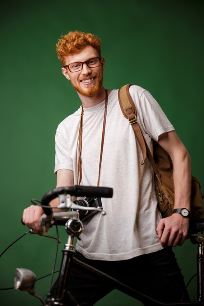 Readhead alegre jovem barbudo hipster com mochila e câmera retro, de pé na bicicleta