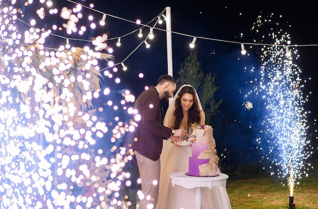 Recém-casados na celebração noturna do bolo de corte de casamento ao ar livre