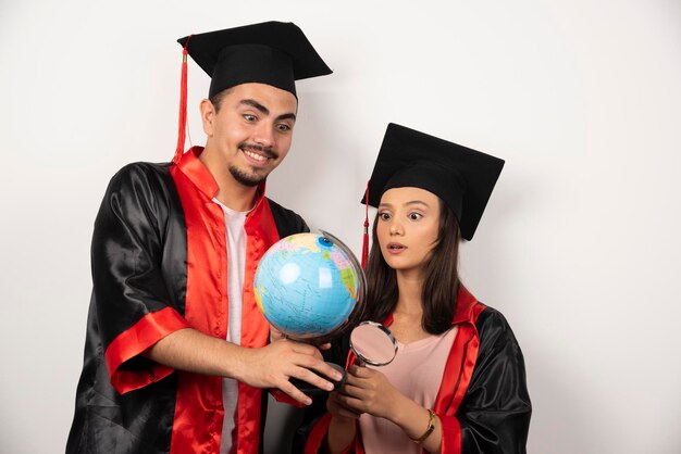 Recém-formados em vestido olhando globo em branco.