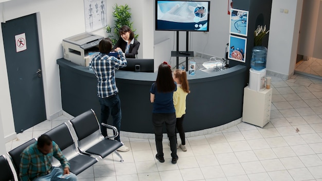 Recepção hospitalar movimentada e sala de espera com diversos pacientes, tendo consulta médica para consulta de check-up. Esperando no saguão da clínica para comparecer à consulta de saúde, suporte de medicamentos.