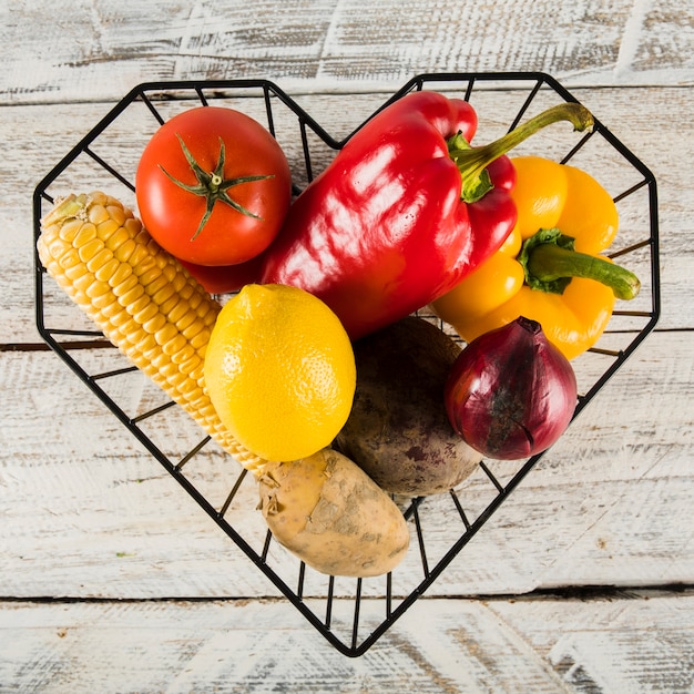 Recipiente de forma de coração com vegetais crus coloridos sobre fundo de madeira