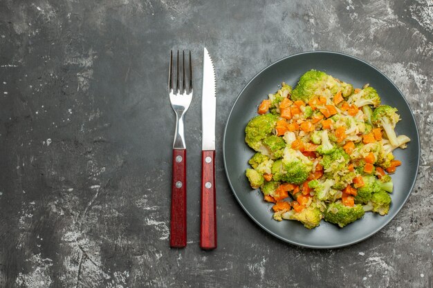 Refeição saudável com brocoli e cenoura em uma placa preta com garfo e faca em imagens de mesa cinza