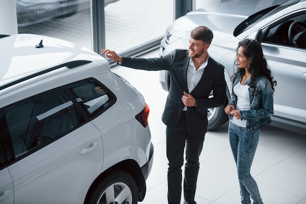 Reflexo de pessoas no vidro. Cliente do sexo feminino e empresário barbudo elegante e moderno no salão automóvel