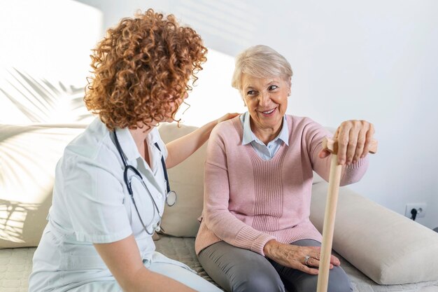 Relação amigável entre o cuidador sorridente de uniforme e mulher idosa feliz Apoiadora jovem enfermeira olhando para mulher sênior Jovem cuidador adorável e ala feliz