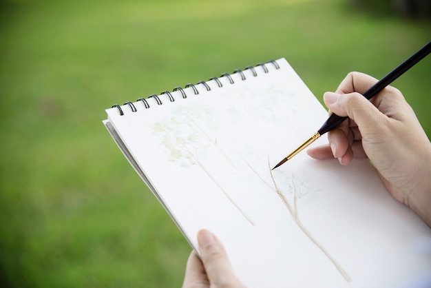 Relaxe a mulher pintando o trabalho de arte em aquarela na natureza da floresta de jardim verde