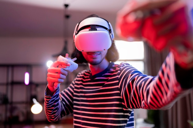 Relaxe o homem adulto asiático usando fone de ouvido de realidade virtual e segurando controladores Joga em um esporte de boxe Videogame em casa Jogando um jogo de esporte ativo VR online na sala de estar com ambiente de iluminação rgb
