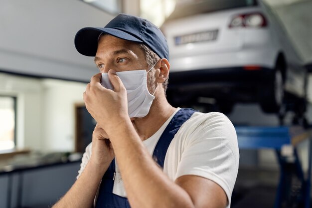 Reparador de automóveis ajustando a máscara facial em uma oficina devido à pandemia COVID19