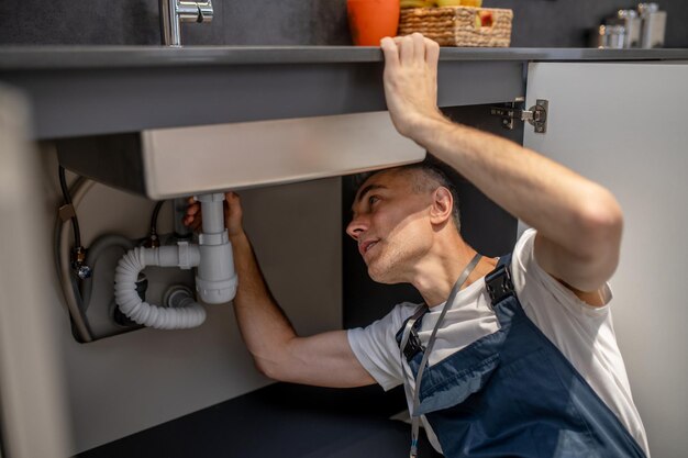 Reparo de encanador Homem de meia idade atento experiente examinando o fundo da pia da cozinha