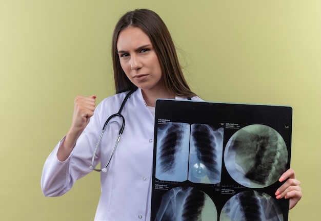 Foto grátis restrita jovem médica usando estetoscópio jaleco segurando um raio-x sobre fundo verde