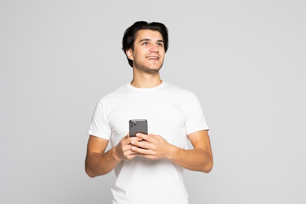 Retrato à luz do dia de um jovem europeu europeu isolado no cinza, vestindo branco com smartphone
