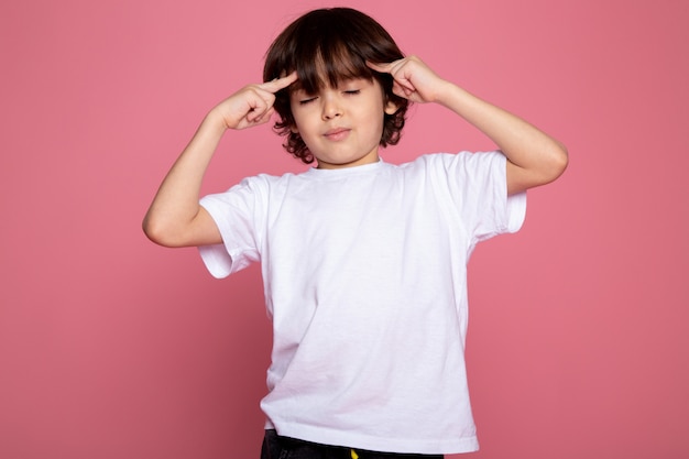 Retrato adorável bonito de menino criança em camiseta branca e calça preta na mesa-de-rosa