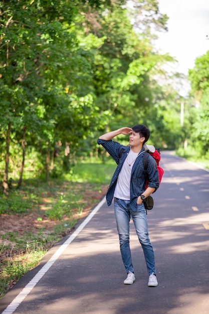 Retrato alegre jovem com mochila em pé e sorrindo na trilha da floresta, copie o espaço