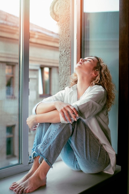 Retrato analógico de uma linda mulher posando dentro de casa em um peitoril da janela