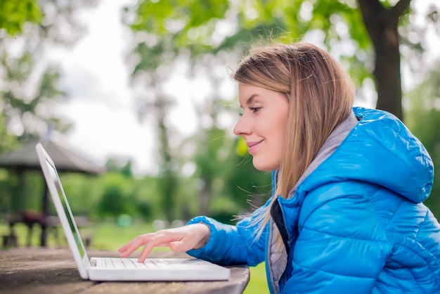 Retrato ao ar livre da jovem mulher no parque com laptop.