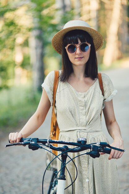 Retrato ao ar livre de atraente jovem morena de chapéu em uma bicicleta.