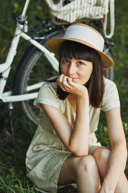 Retrato ao ar livre de atraente jovem morena de chapéu em uma bicicleta.