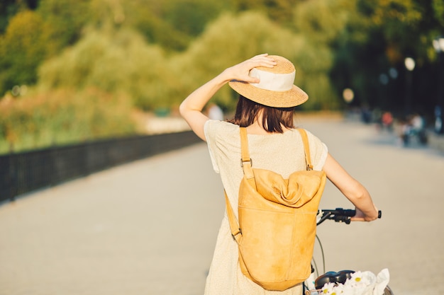 Retrato ao ar livre de atraente jovem morena de chapéu em uma bicicleta.