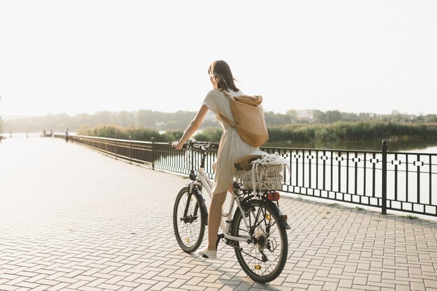 Retrato ao ar livre de atraente jovem morena de chapéu em uma bicicleta.