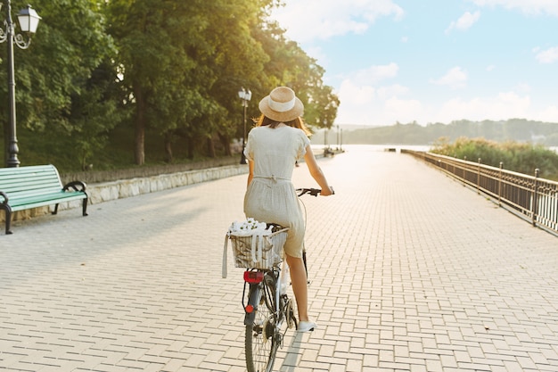 Retrato ao ar livre de atraente jovem morena de chapéu em uma bicicleta.