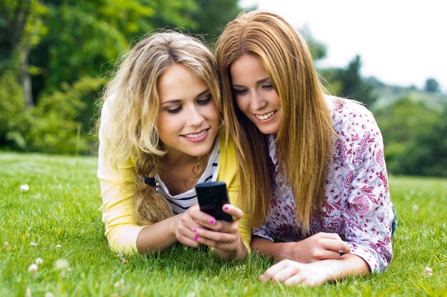 Retrato ao ar livre de duas lindas mulheres jovens com celular no parque