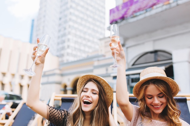 Retrato ao ar livre de garotas loiras felizes posando com taças de vinho cheias de champanhe