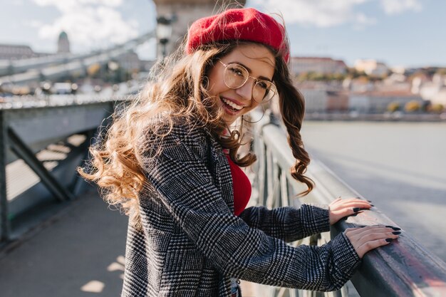 Retrato ao ar livre de glamourosa turista feminina olhando por cima do ombro na ponte