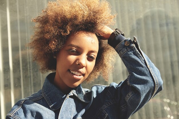 Retrato ao ar livre de uma jovem elegante de pele escura com cabelo encaracolado e jaqueta jeans
