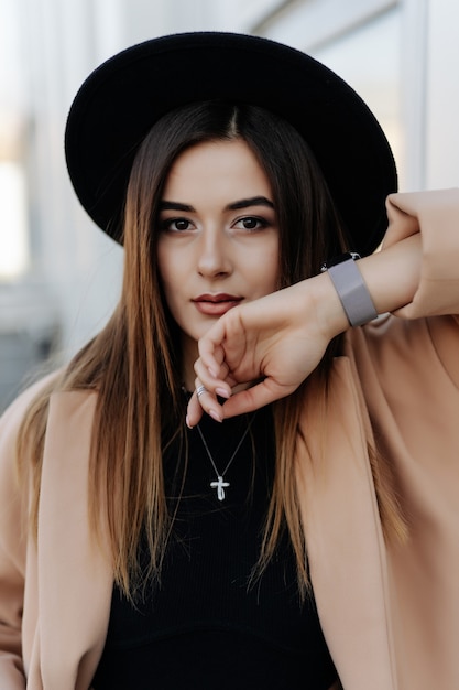 Retrato ao ar livre de uma jovem mulher bonita usando um elegante casaco de pele preto e chapéu de aba larga.