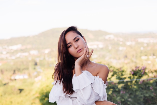 Retrato ao ar livre de uma mulher asiática com vestido branco usando colar e brincos