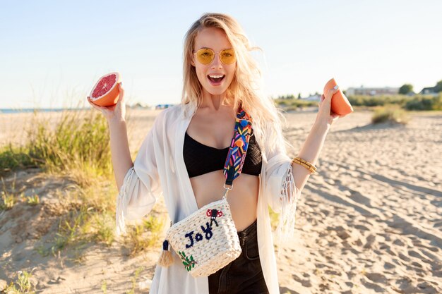 Retrato ao ar livre do estilo de vida da mulher despreocupada brincalhão, posando com saborosas metades de toranja nas mãos.