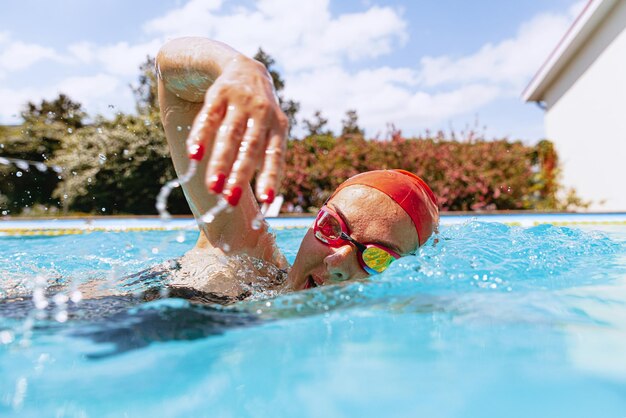 Retrato ao vivo de jovem nadadora em touca e praticando em piscina pública ao ar livre